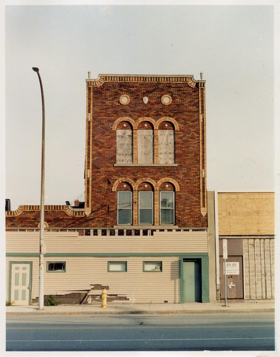 A brick building with boarded-up arched windows stands next to a street light and a yellow fire hydrant.