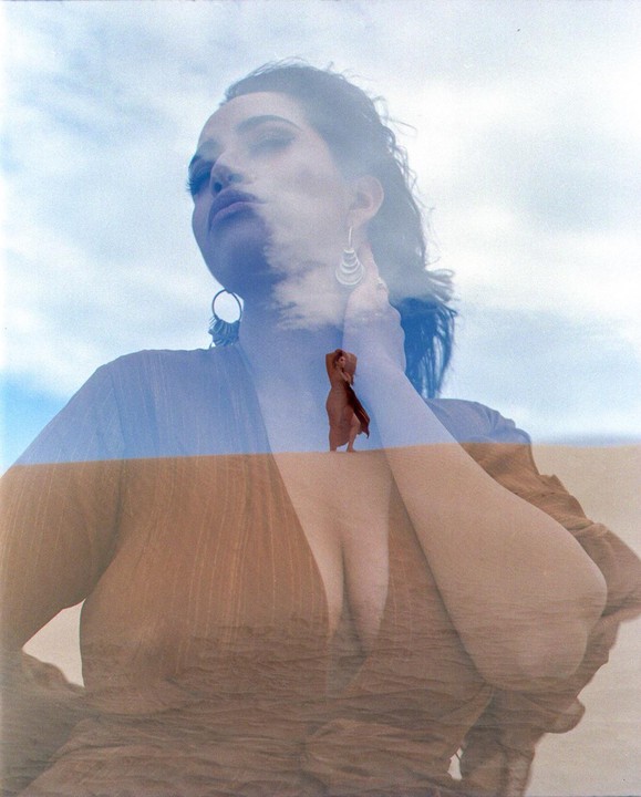 A double exposure shows a woman's face and chest superimposed over a desert landscape with a small figure of a woman in the distance.