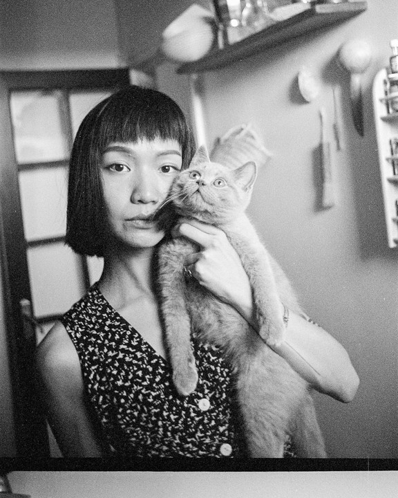 A woman with short hair holds a cat looking upwards.