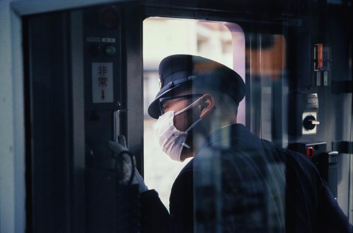 A man in uniform and a face mask looks out a train window.