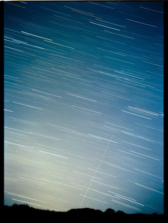 Star trails streak across the night sky above a silhouetted landscape.