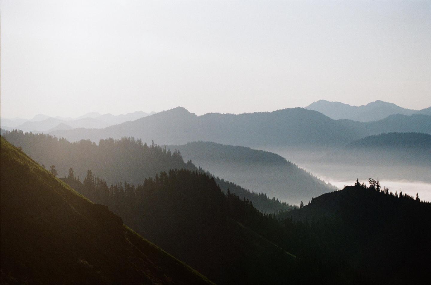 A hazy mountain landscape shows layers of forested hills with fog in the valleys.