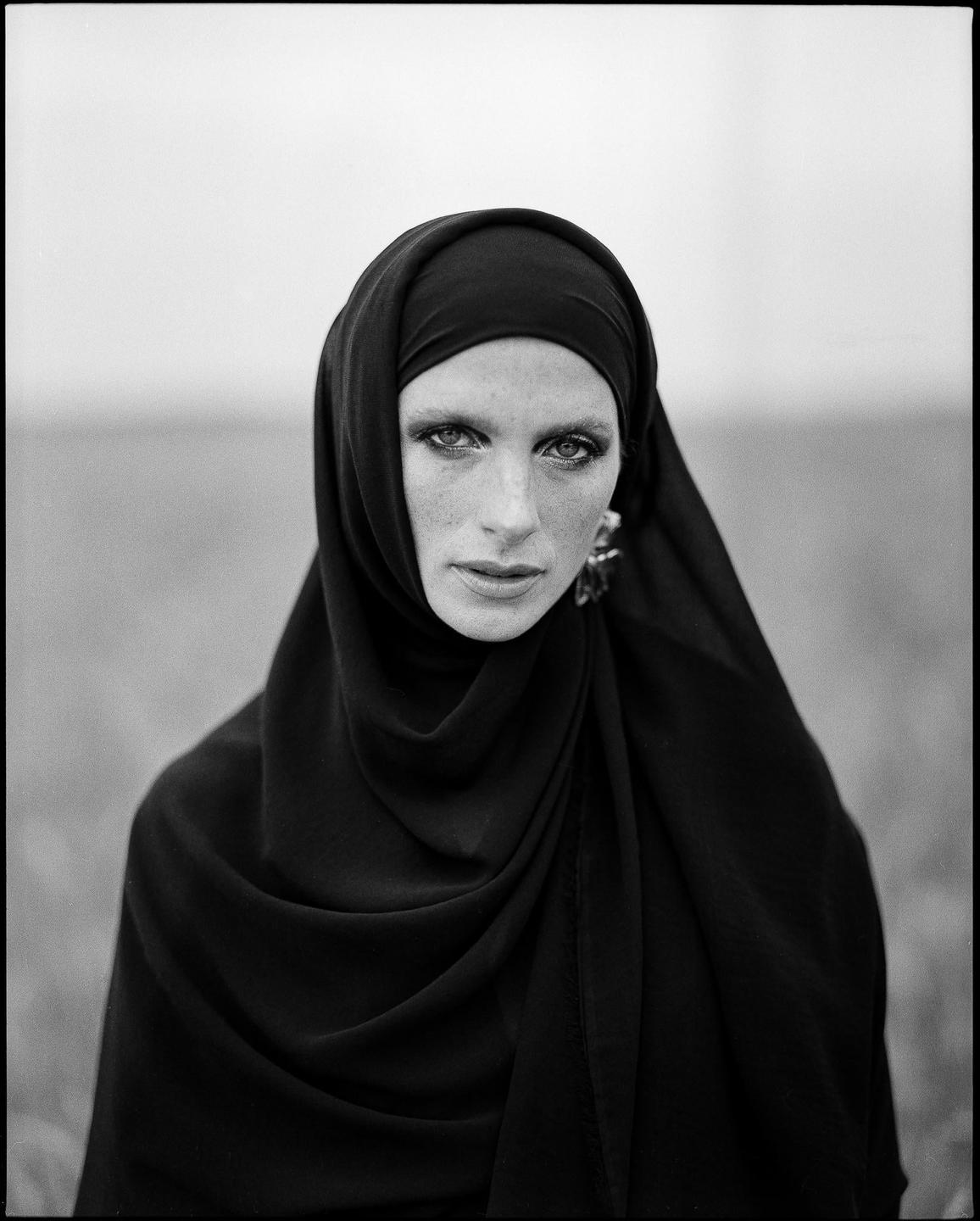 A woman wearing a hijab looks directly at the viewer.