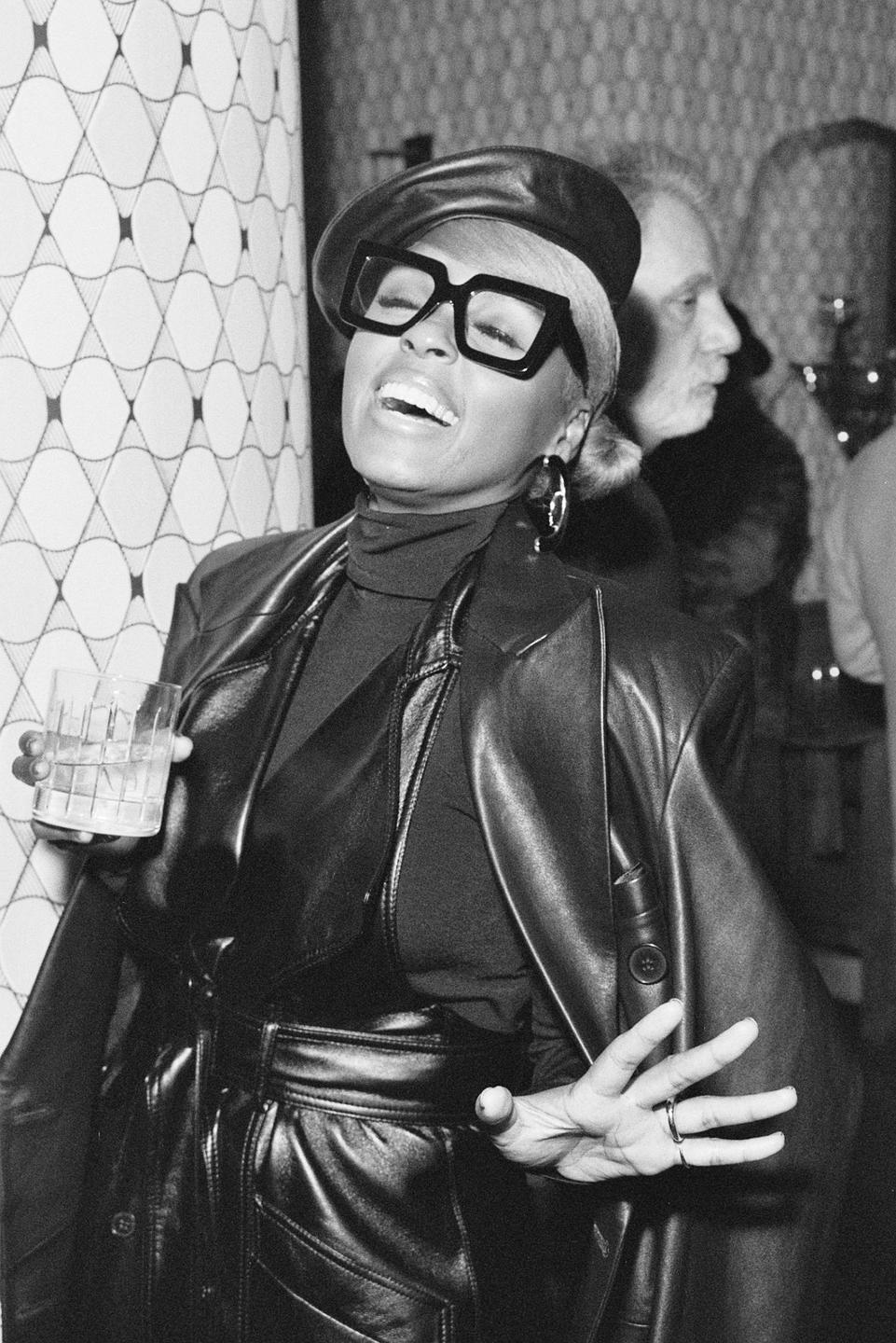 A woman wearing a beret and glasses is holding a drink and laughing.