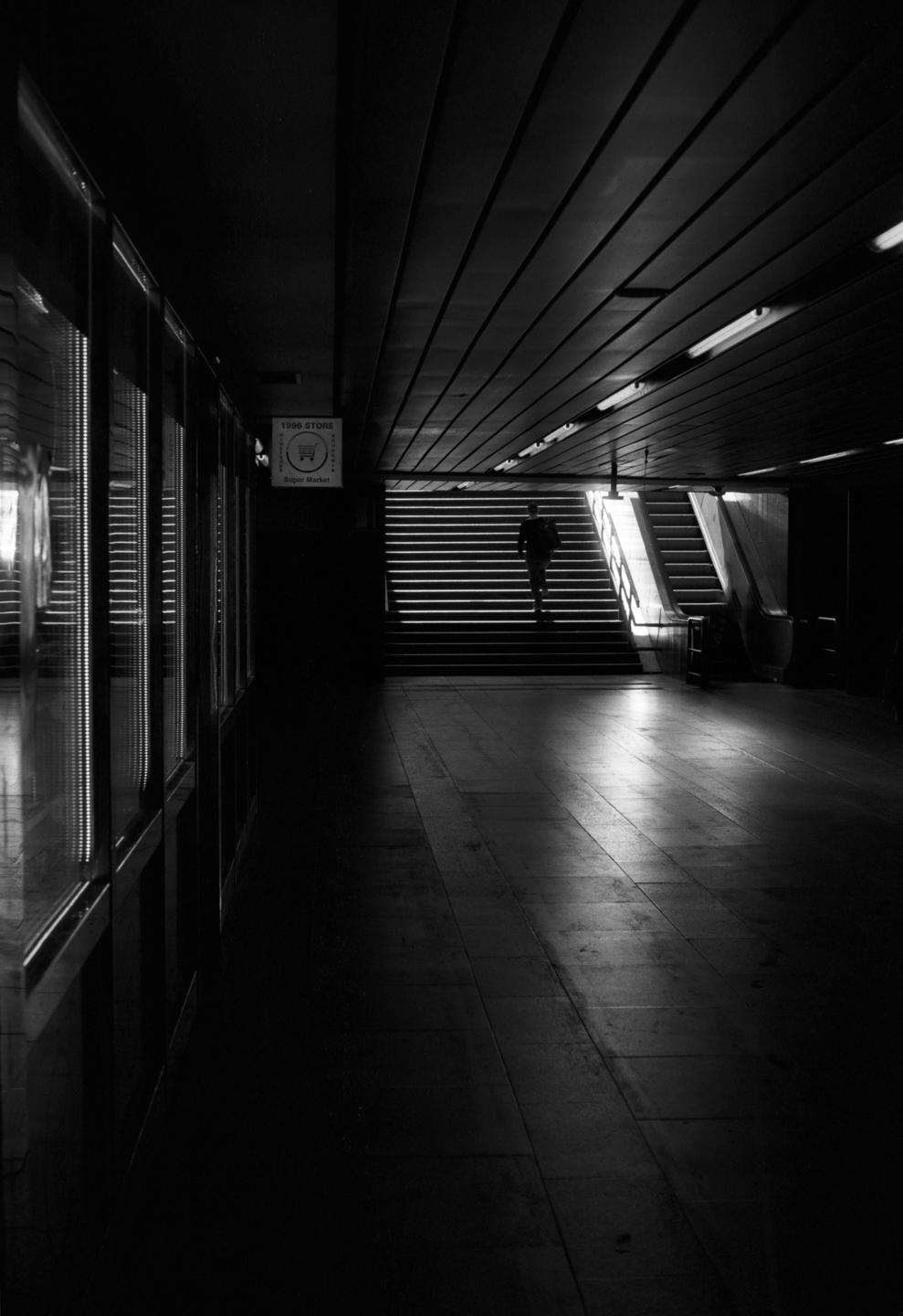 A man walks up a brightly lit staircase in a dark underground passage.