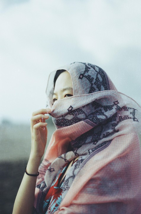 A woman with a patterned scarf covering her face looks directly at the viewer.