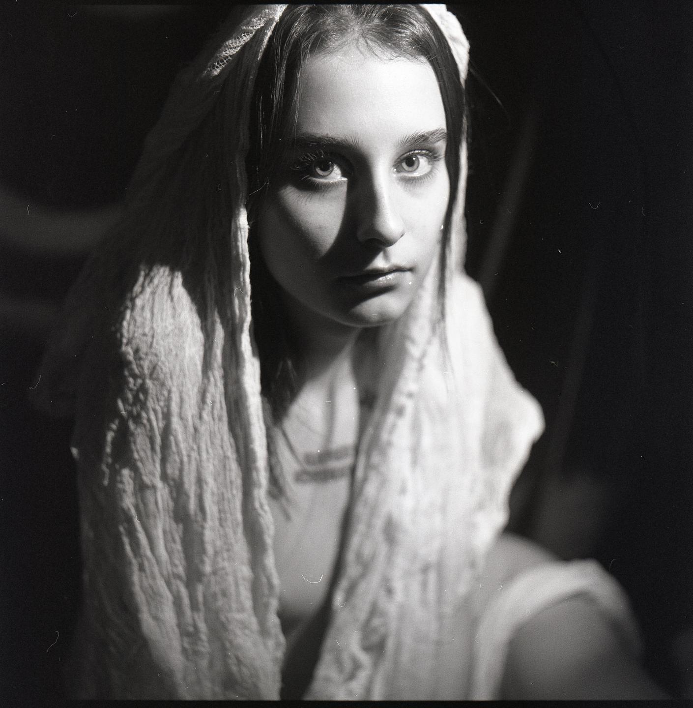 A woman with a white head covering looks directly at the viewer.