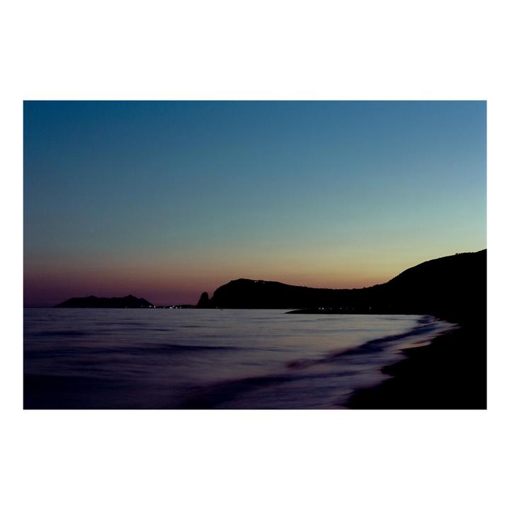 A long exposure photograph captures the coastline and sea at dusk with a gradient sky.