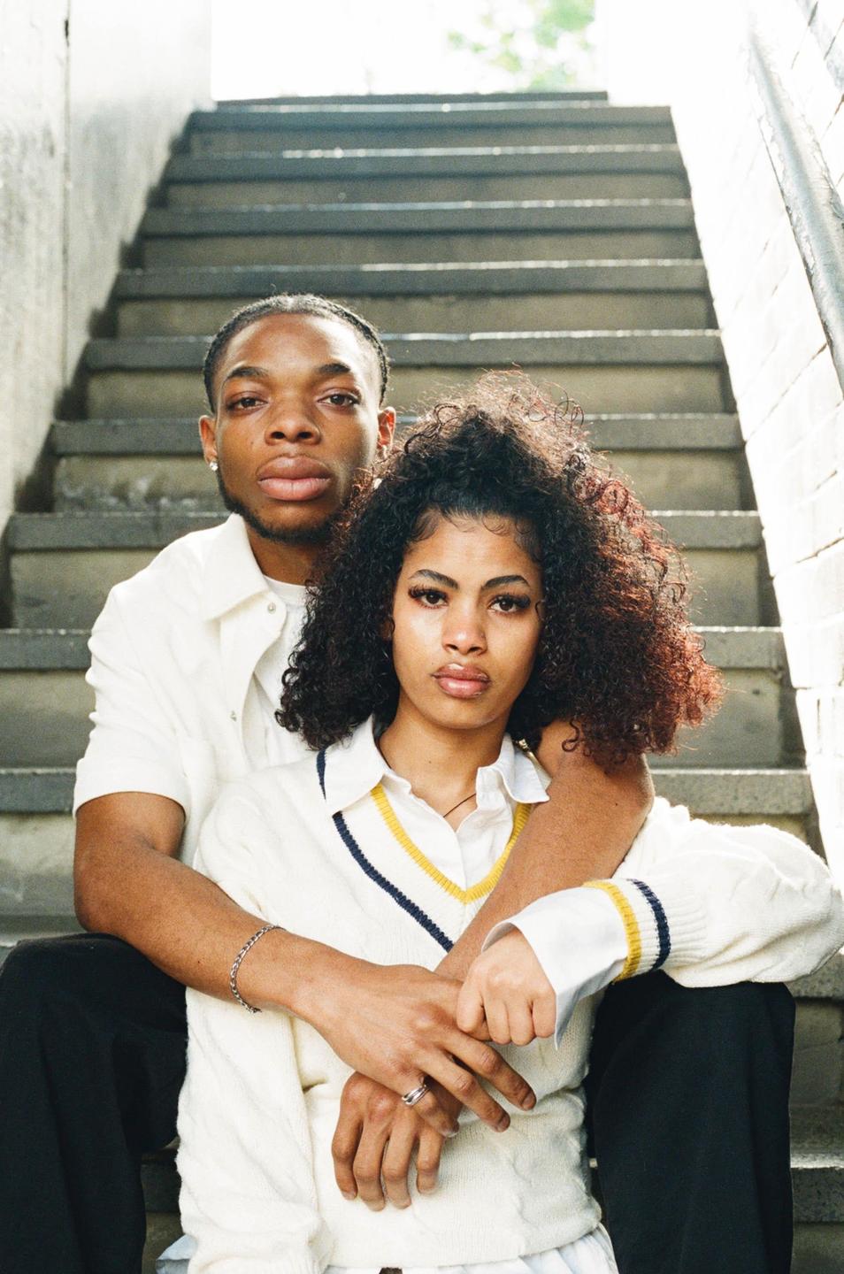 A couple sits on concrete steps, with the man embracing the woman from behind.