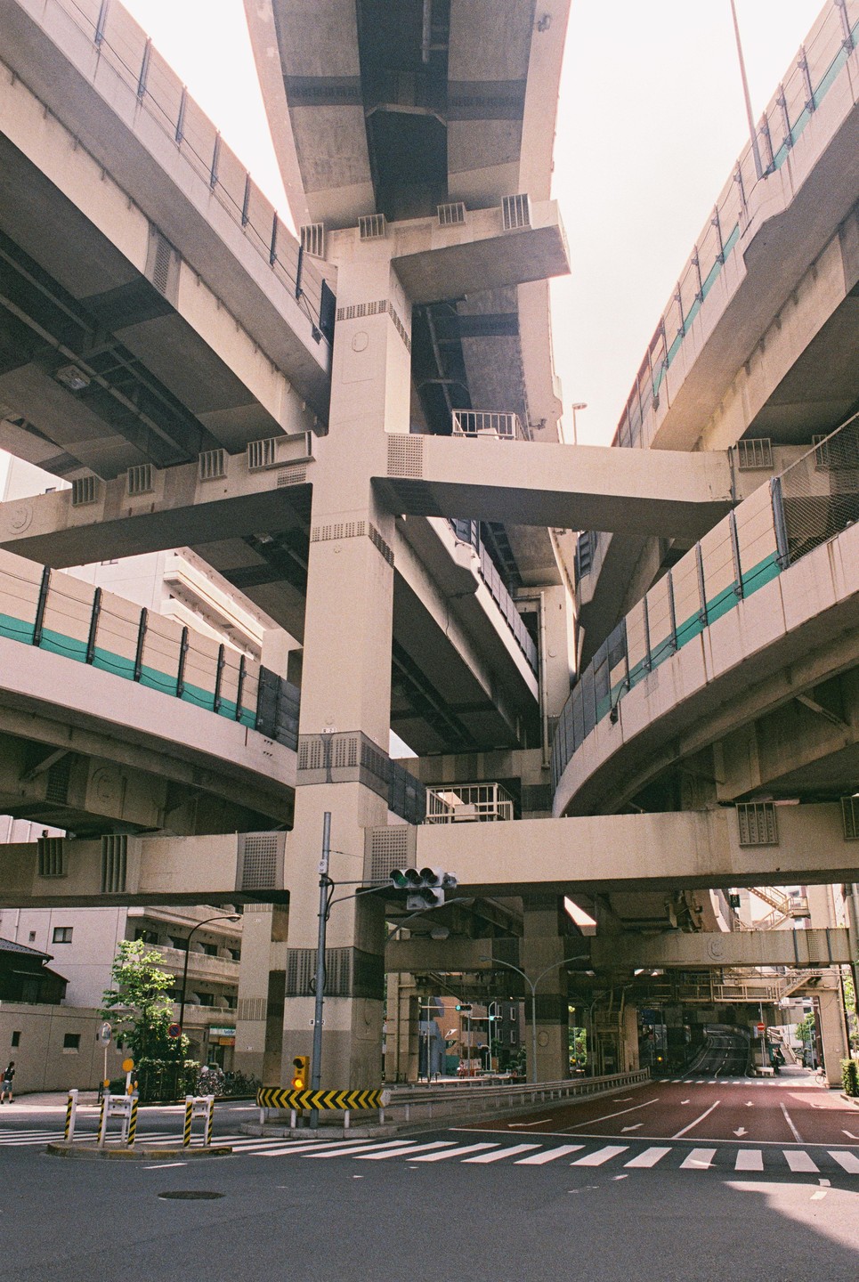 A complex network of elevated highways and ramps intersects above a city street with a crosswalk and traffic lights.