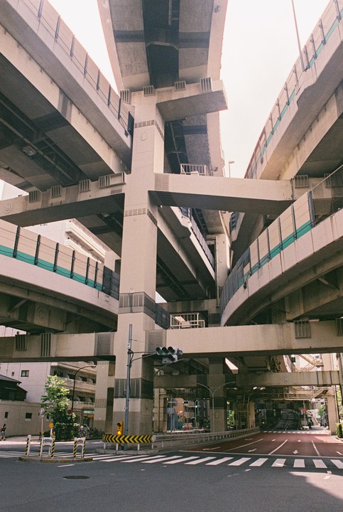 A complex network of elevated highways and ramps intersects above a city street with a crosswalk and traffic lights.