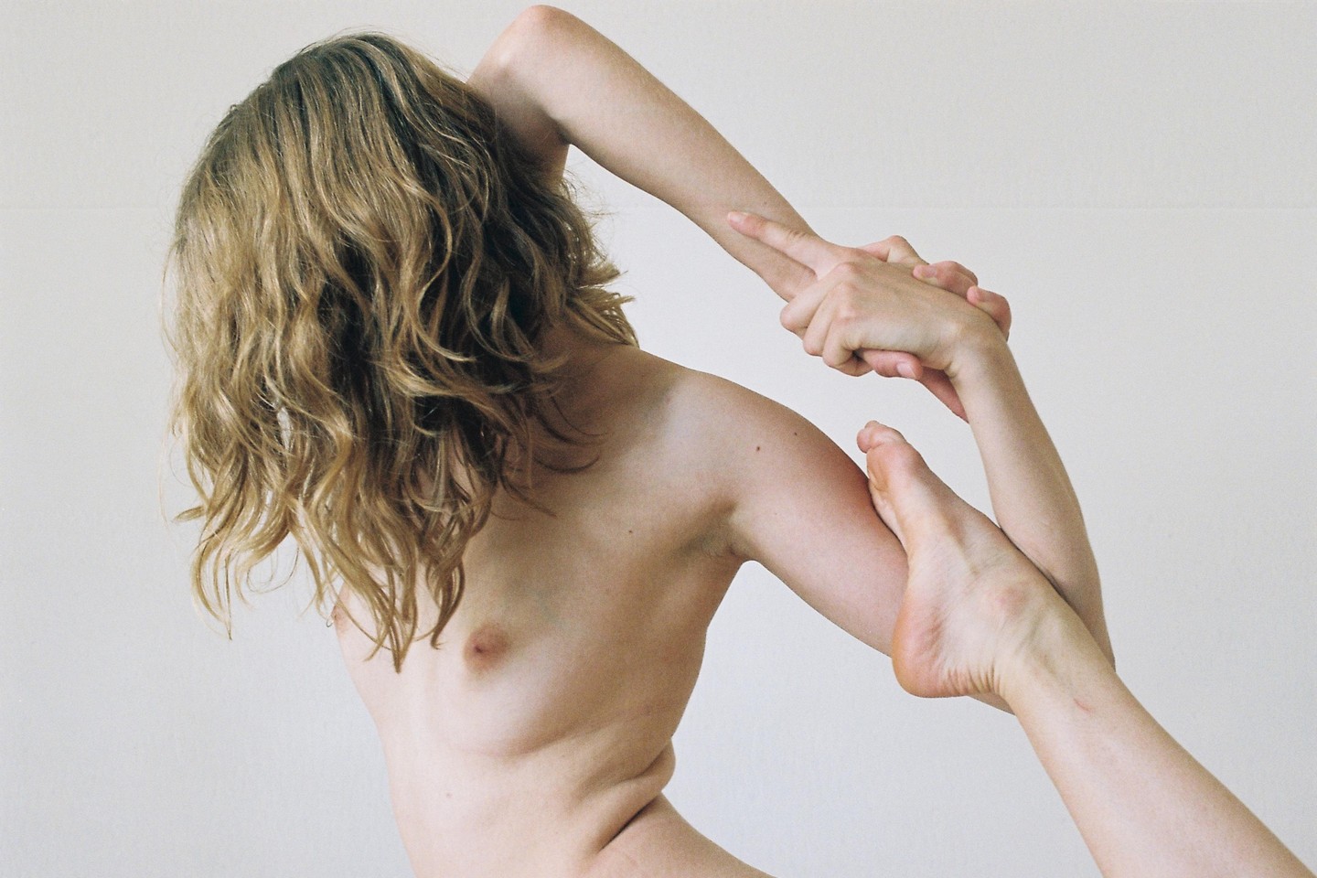 A woman with long wavy hair is shown from the back, holding her foot with her hands in a yoga pose.