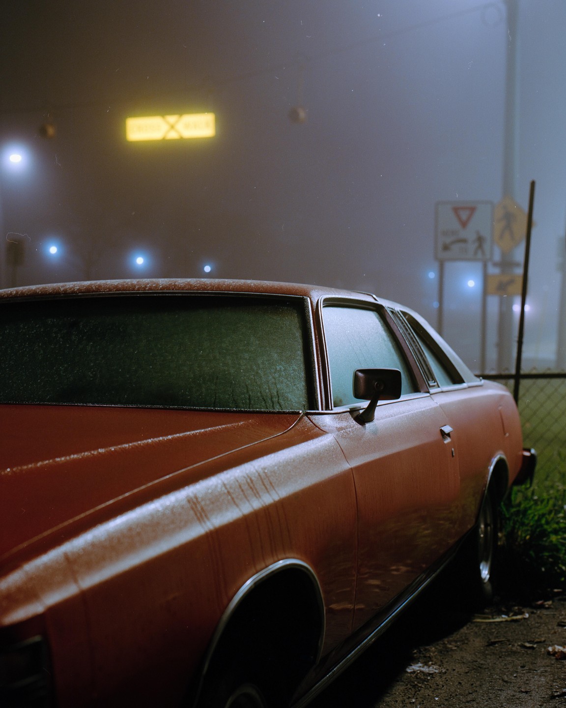 A red car is parked on a foggy night with streetlights and signs visible in the background.