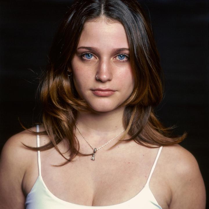 A young woman with blue eyes and brown hair looks directly at the viewer.
