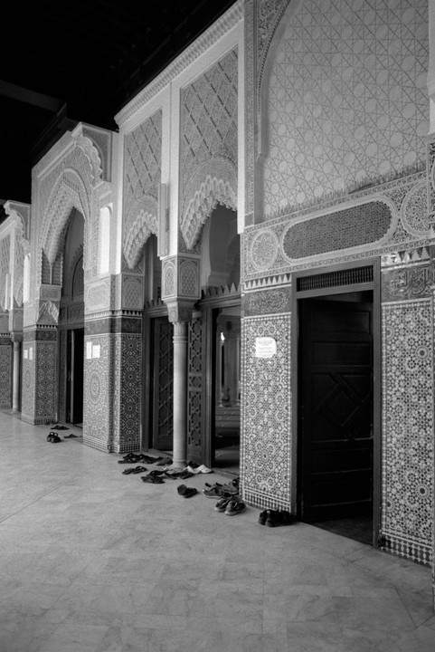 A row of ornate arched doorways with shoes scattered on the floor in front of them.