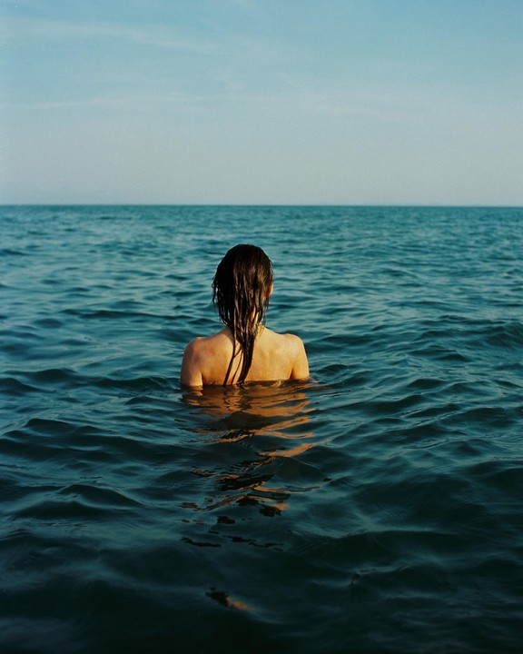 A woman with wet hair is swimming in the ocean, looking out towards the horizon.