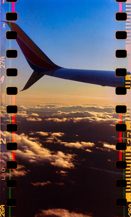 An airplane wing is visible above clouds during sunset.