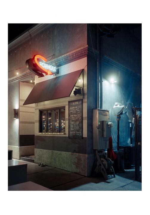 A neon sign for "FOXHOLE" illuminates the facade of a building at night.
