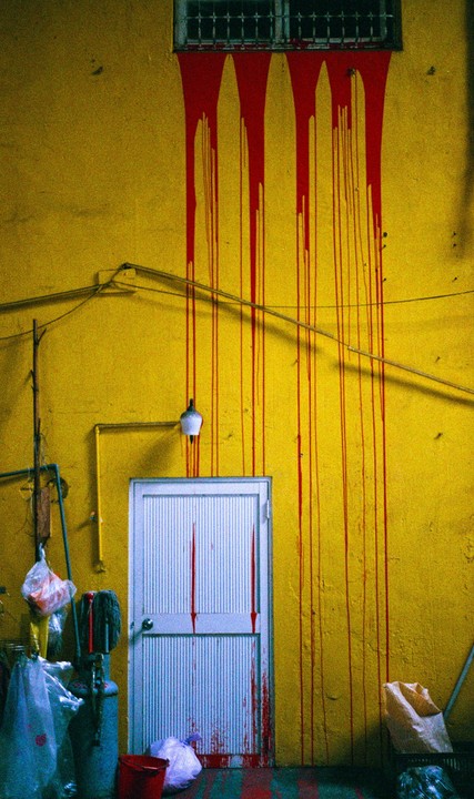 Red paint drips down a bright yellow wall and across a white door.