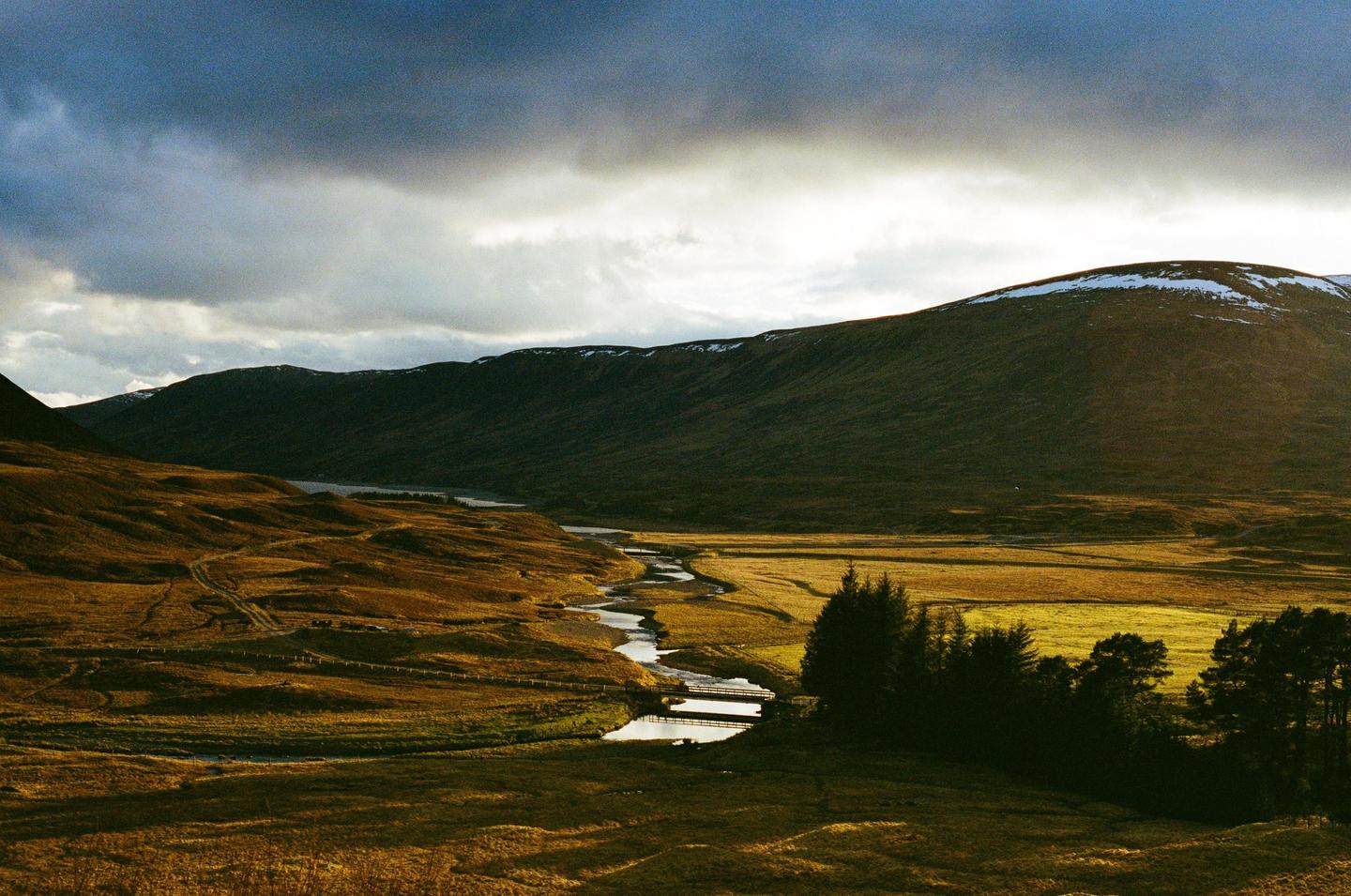 A winding river flows through a valley with mountains under a cloudy sky.