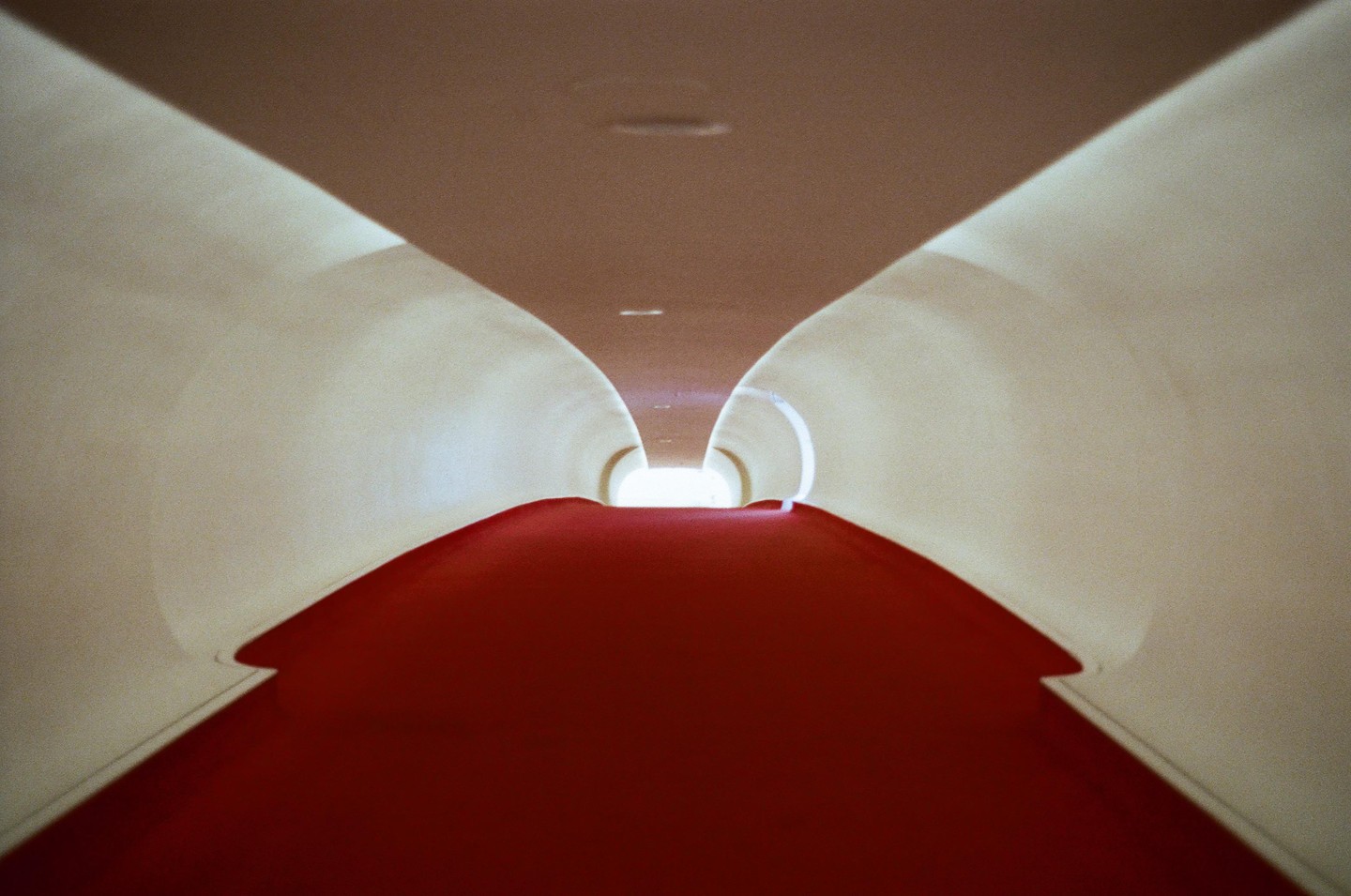 A long, curved hallway with a red carpet leads to a bright light at the end.