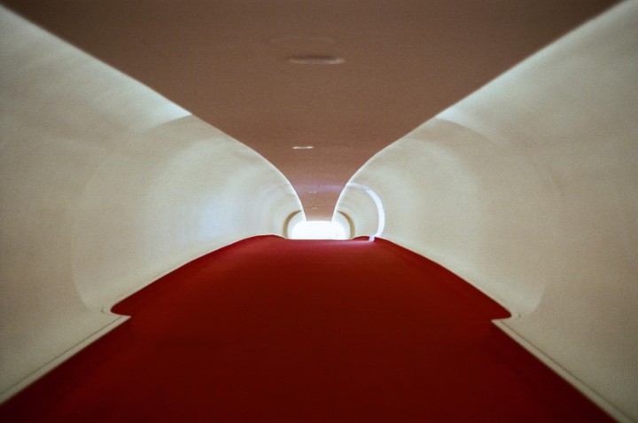 A long, curved hallway with a red carpet leads to a bright light at the end.