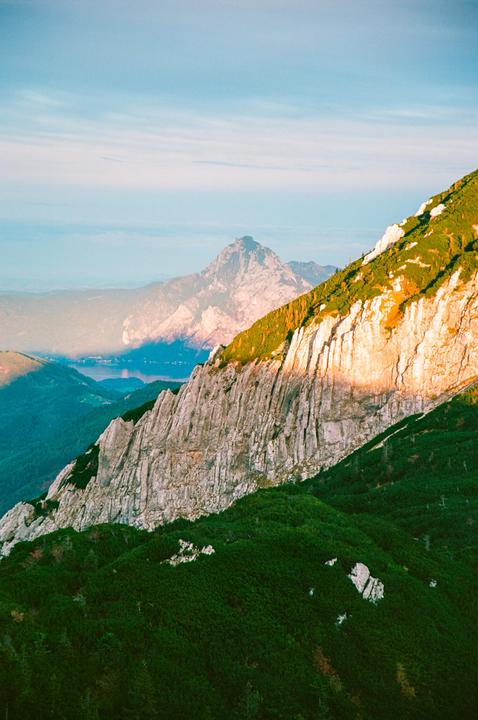 A mountain landscape shows a rocky peak in the distance and a sunlit cliff face in the foreground.