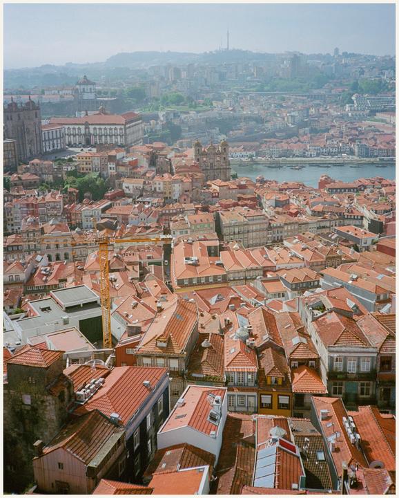 A hazy aerial view shows a dense city with red-tiled roofs and a river.