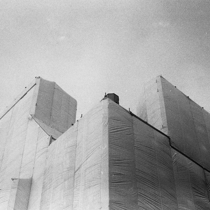 A building under construction is covered in white tarps against a bright sky.