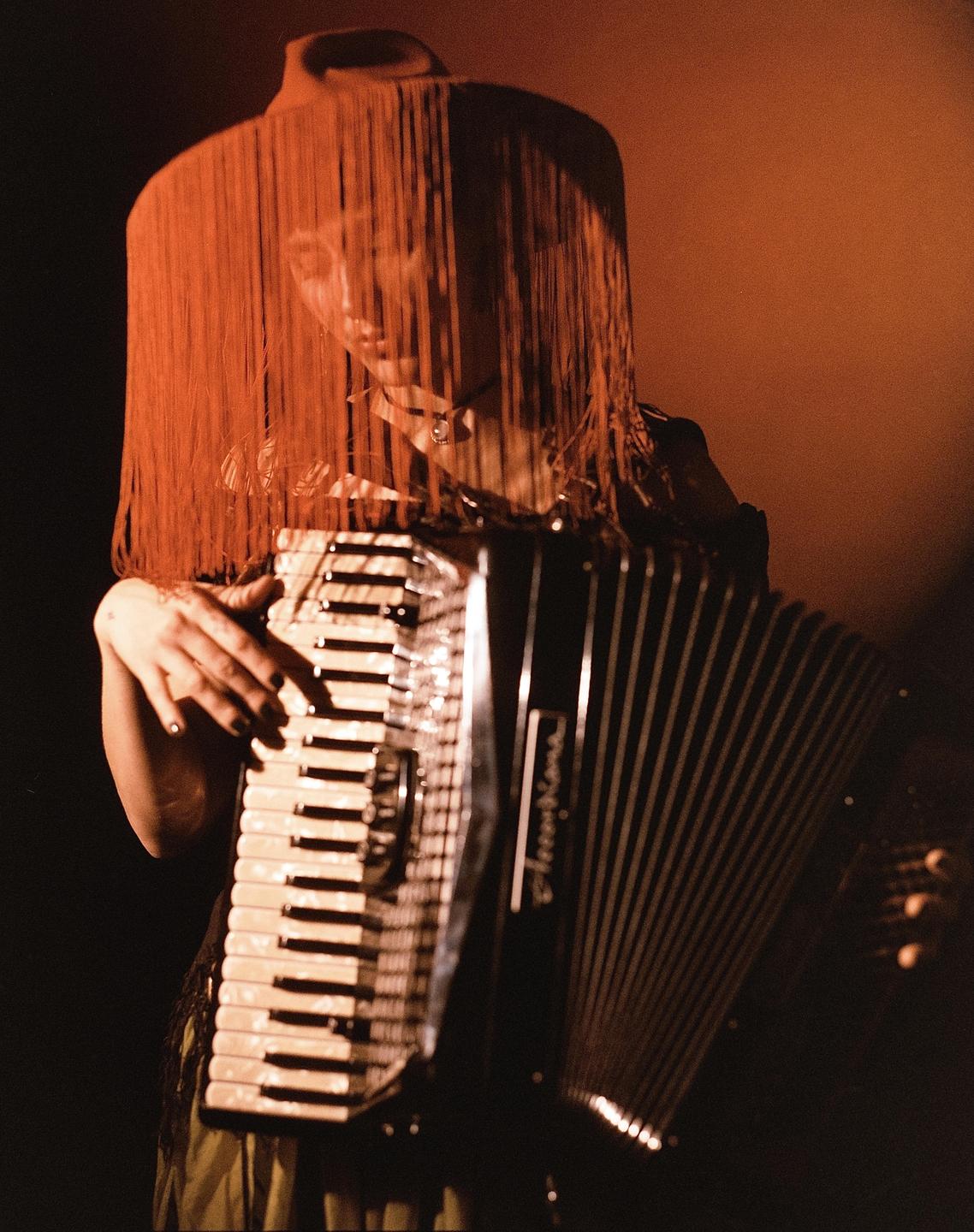 A woman wearing a fringed hat plays an accordion.