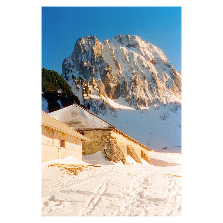 A snow-covered mountain rises behind a building with a snow-covered roof and a stone wall.
