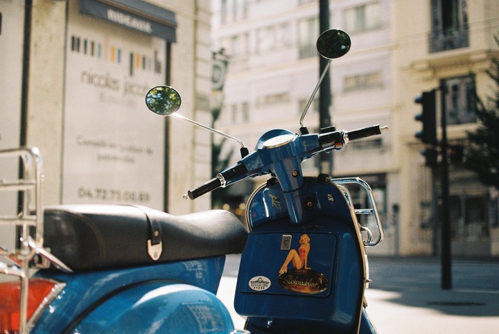 A blue scooter with a pin-up sticker is parked on a city street.