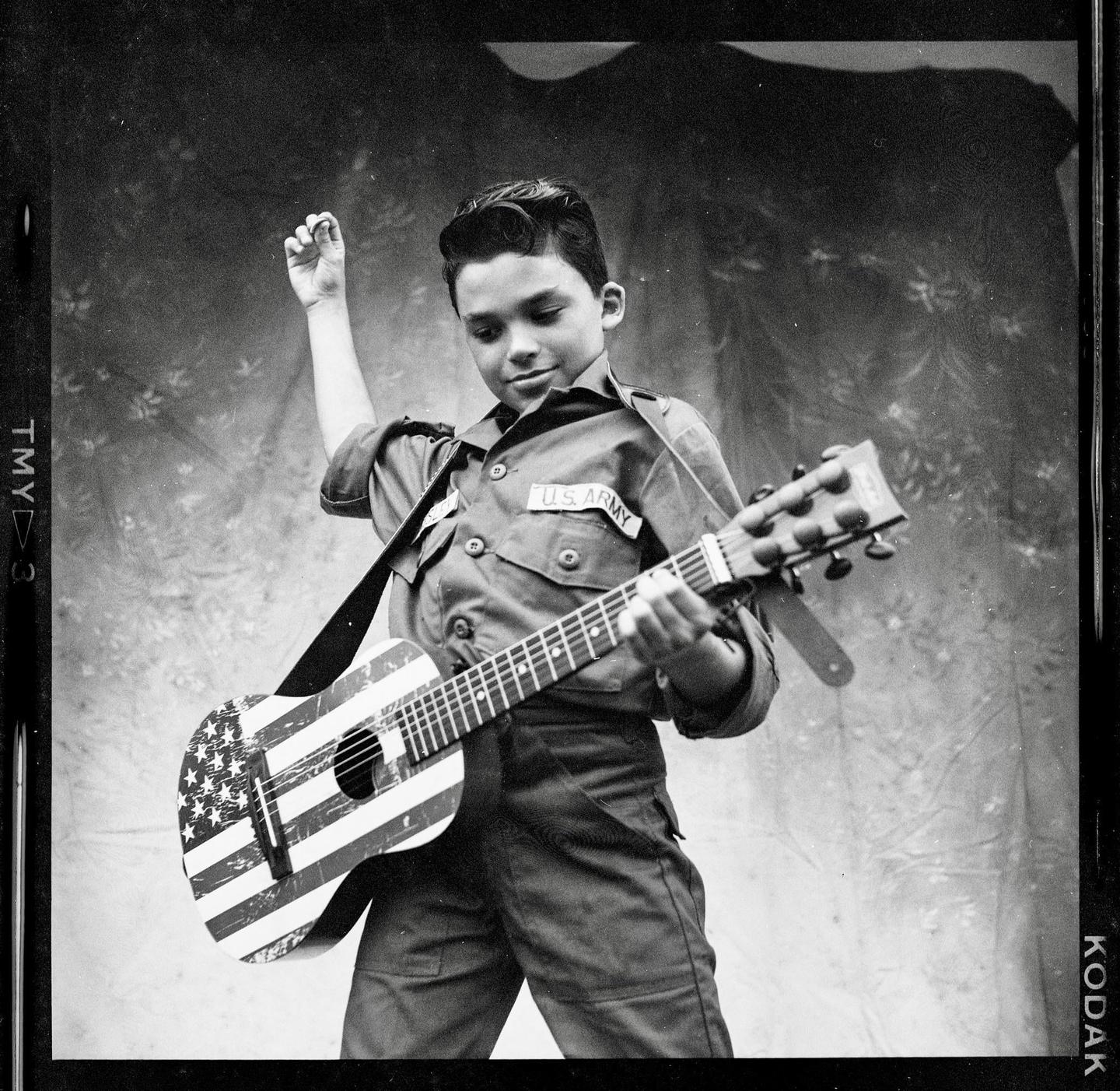 A boy in a U.S. Army uniform plays a guitar painted with the American flag.
