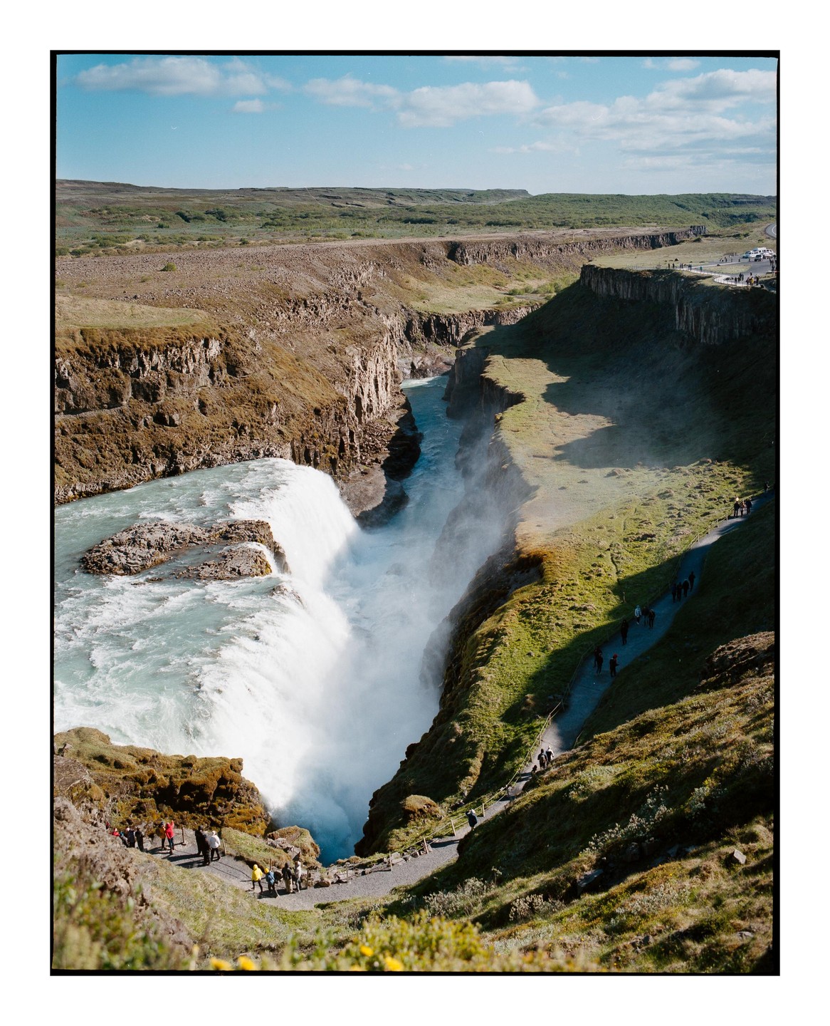 A large waterfall cascades into a canyon with people walking on paths along the edges.