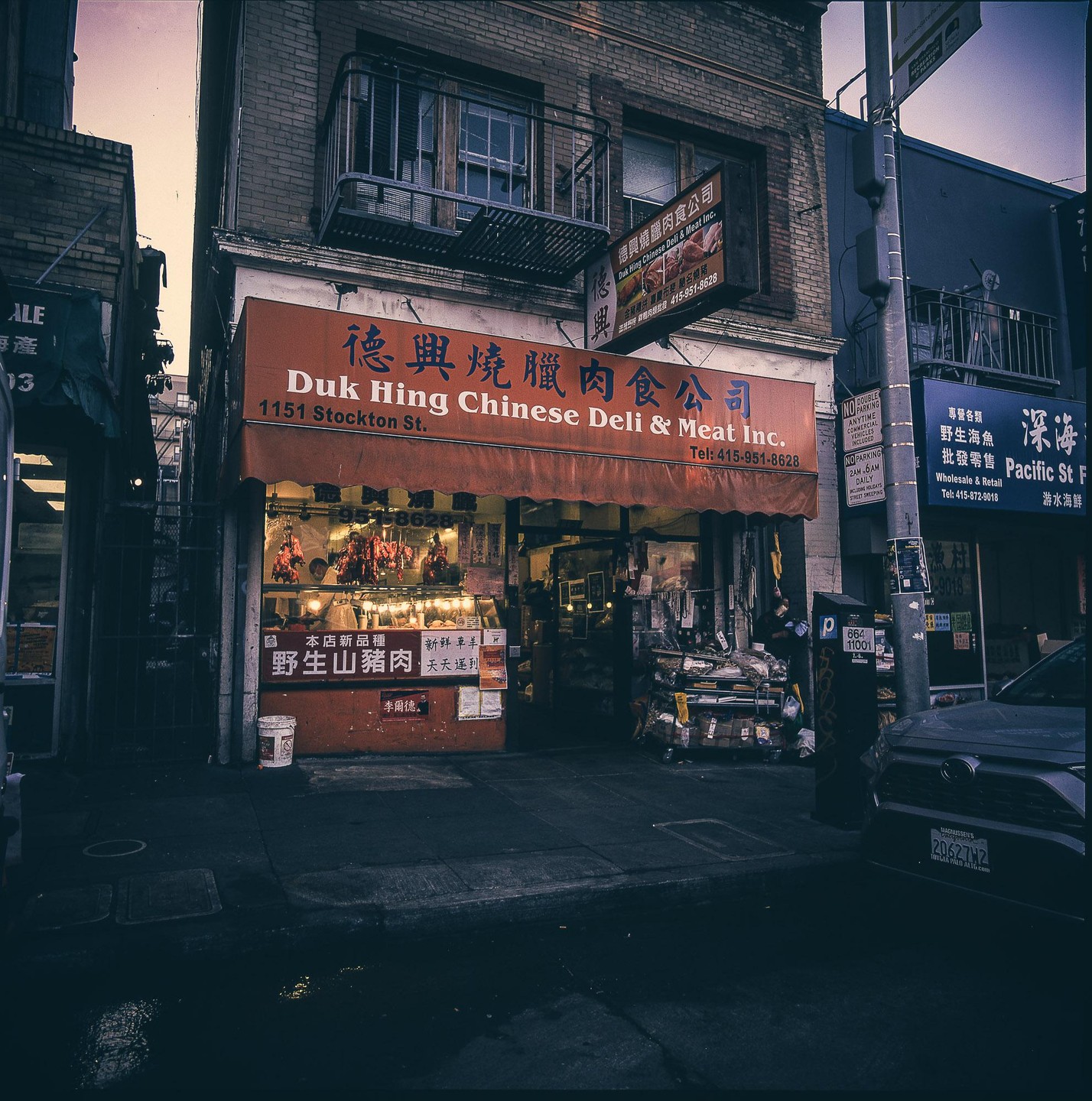 A Chinese deli and meat shop with an orange awning is visible on a street in Chinatown, San Francisco.