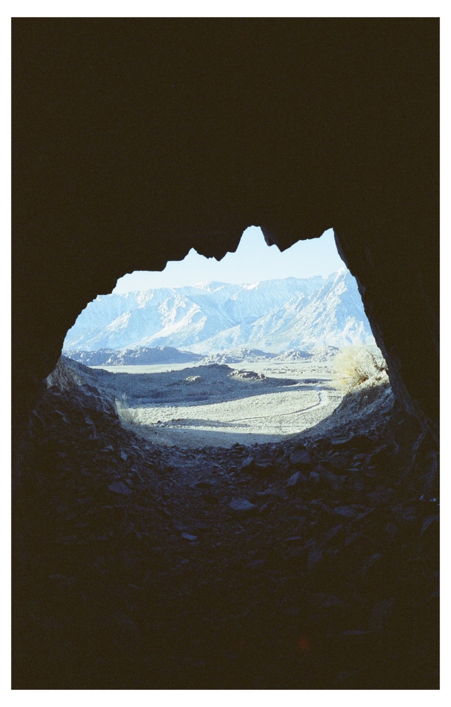 A view of a valley and mountains is seen through a dark cave opening.