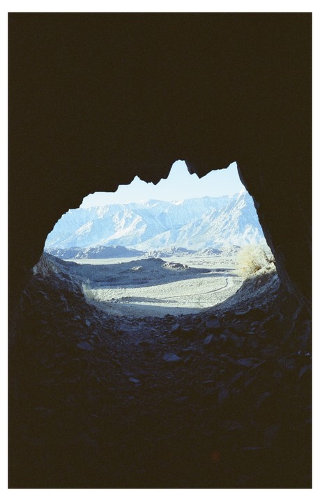 A view of a valley and mountains is seen through a dark cave opening.
