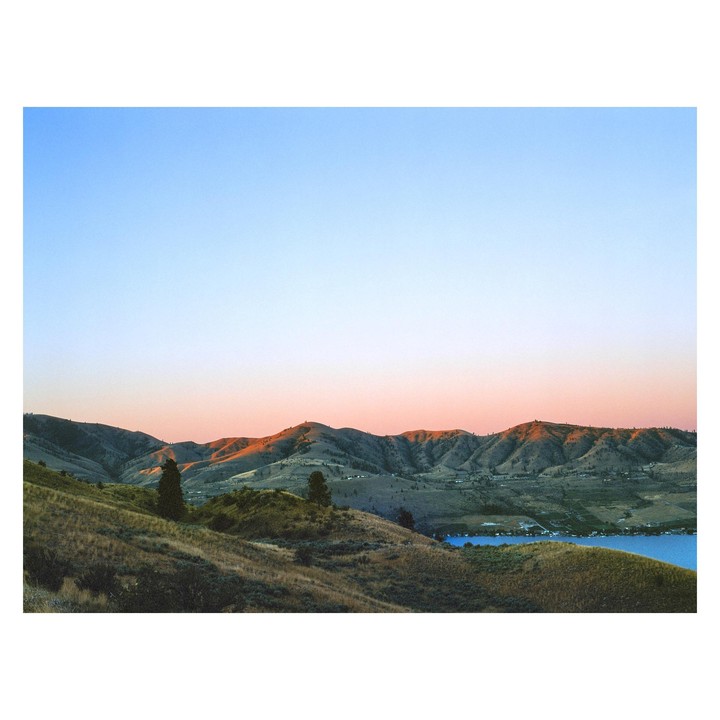 A landscape of rolling hills and a lake at sunset.
