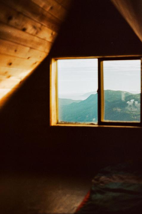 A window in a wooden cabin looks out onto a mountain landscape.