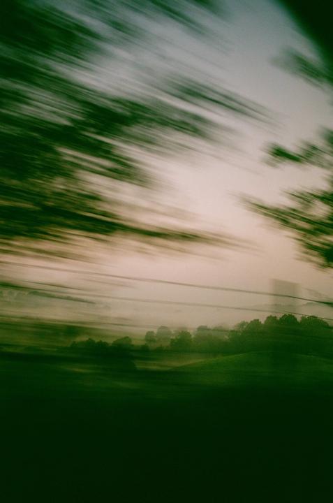 A blurry landscape of green fields and trees is visible under a hazy sky.