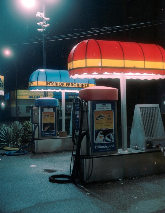 A car wash vending machine with a red and yellow awning stands next to another machine with a blue awning at night.