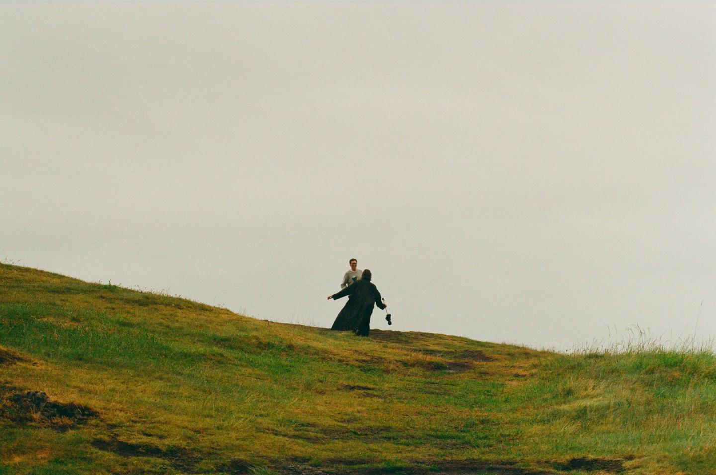 Two men are visible on a grassy hill under a bright sky.