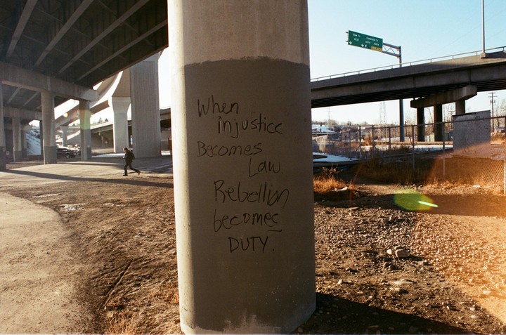 A person runs under a concrete overpass with graffiti on a pillar.