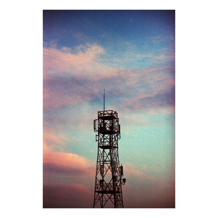 A telecommunications tower stands silhouetted against a sky with pink and blue clouds.