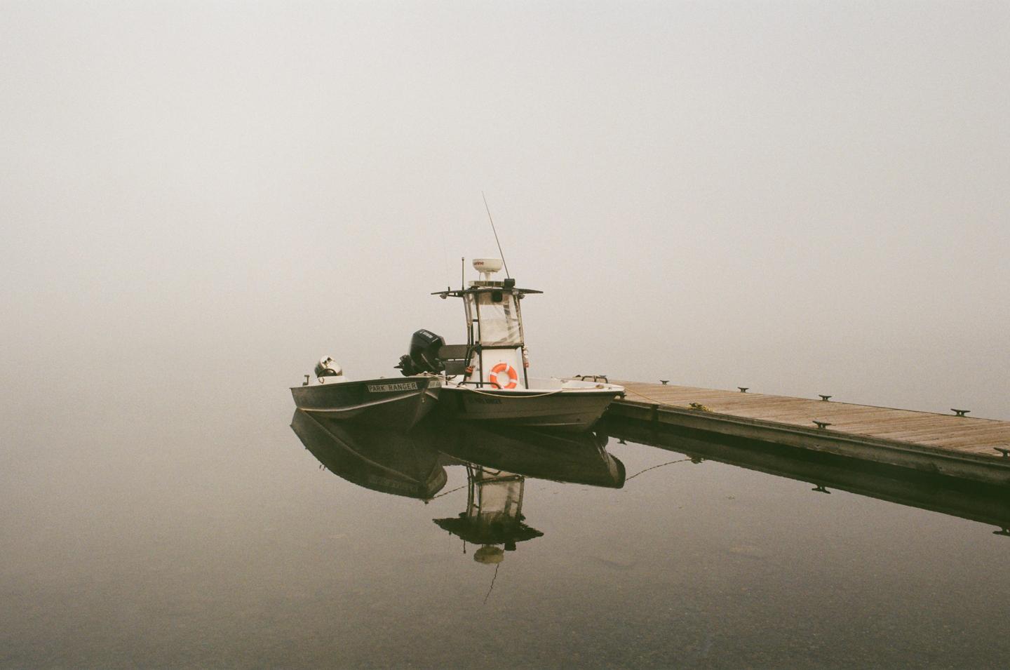 A boat is docked next to a pier on a hazy lake.