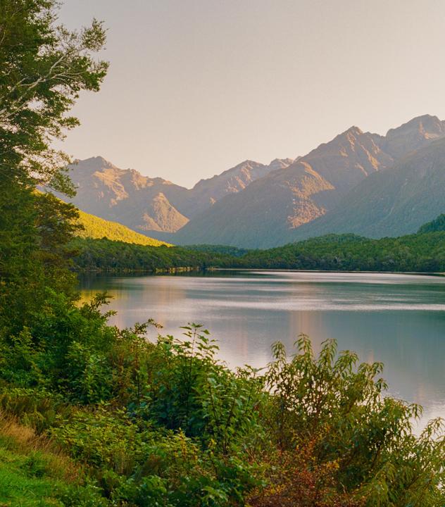 A lake is surrounded by mountains and lush green foliage under a clear sky.