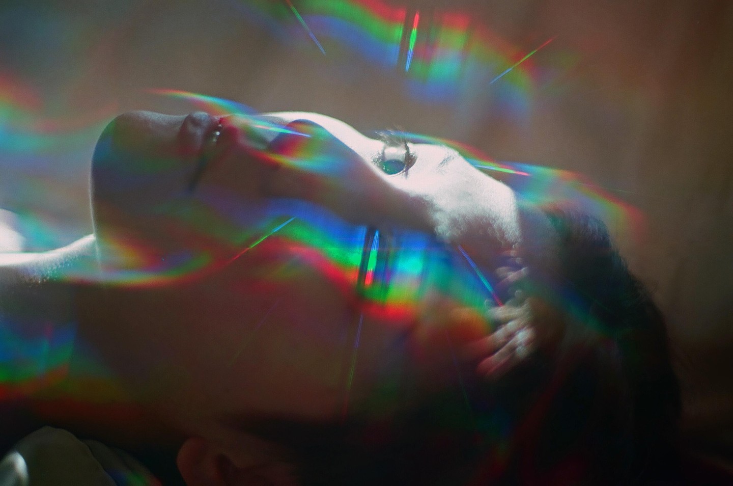 A woman lies with her head tilted back, her face illuminated by colorful light streaks.