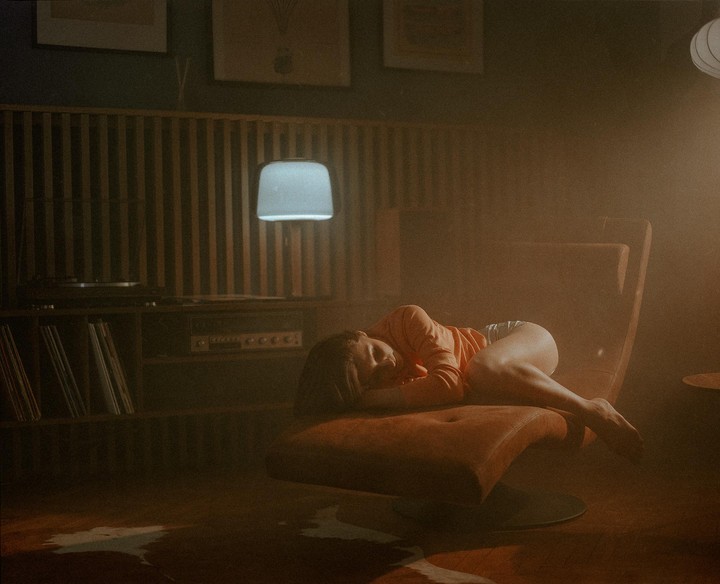 A woman sleeps on an orange lounge chair in a dimly lit room with a record player and records.