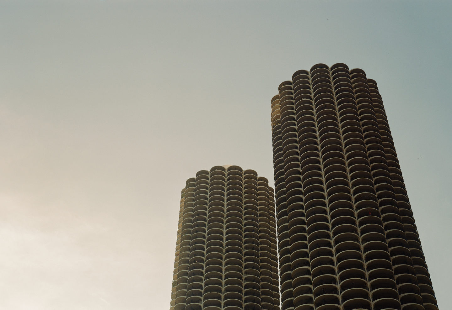 Two cylindrical high-rise buildings with many balconies are visible against a clear sky.