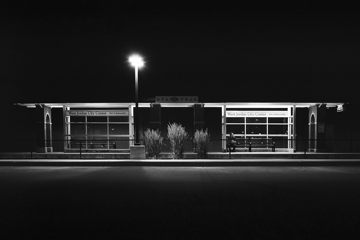 A man sits on a bench at a train station at night.